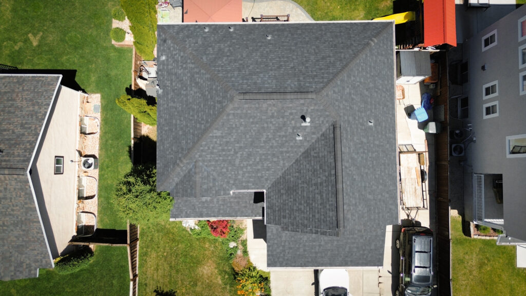 Technician performing roof repair on a leaking section above a Layton - UT attic vent, Roof repair technician in Kaysville - UT examining shingle wear and exposed flashing on a residential slope